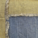 Close-up of Diana's blue linen weave and intersecting gold bands with fringed edges.