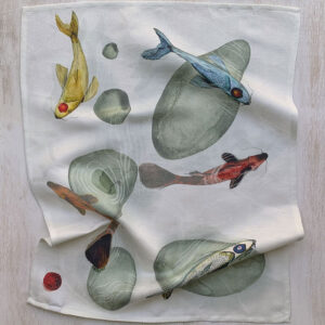 Linen and cotton kitchen towel with multicolour koi carp ink wash illustration laid on a light wood surface — four fish in golden, blue, red and orange among smooth stones