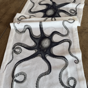 Close-up of the Polipo linen-cotton jacquard table runner with black and gray octopus artwork on an ivory ground