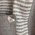 Close-up of heart-shaped button and herringbone linen pocket on grey striped apron.