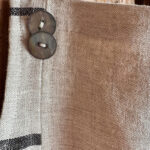 Close-up of two buttons on the natural linen bib of the Follia Pura apron