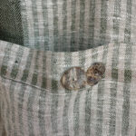 Close-up of the green and ivory striped linen pocket with two decorative buttons on the Follia Pura apron.